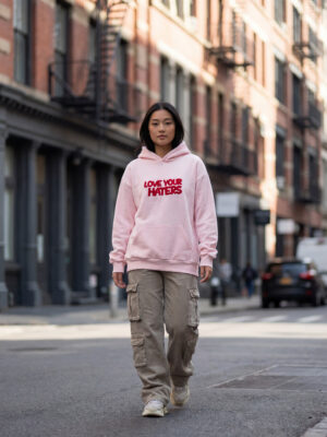 Female model wearing the Love Your Haters Pink Hoodie with embroidered front artwork.